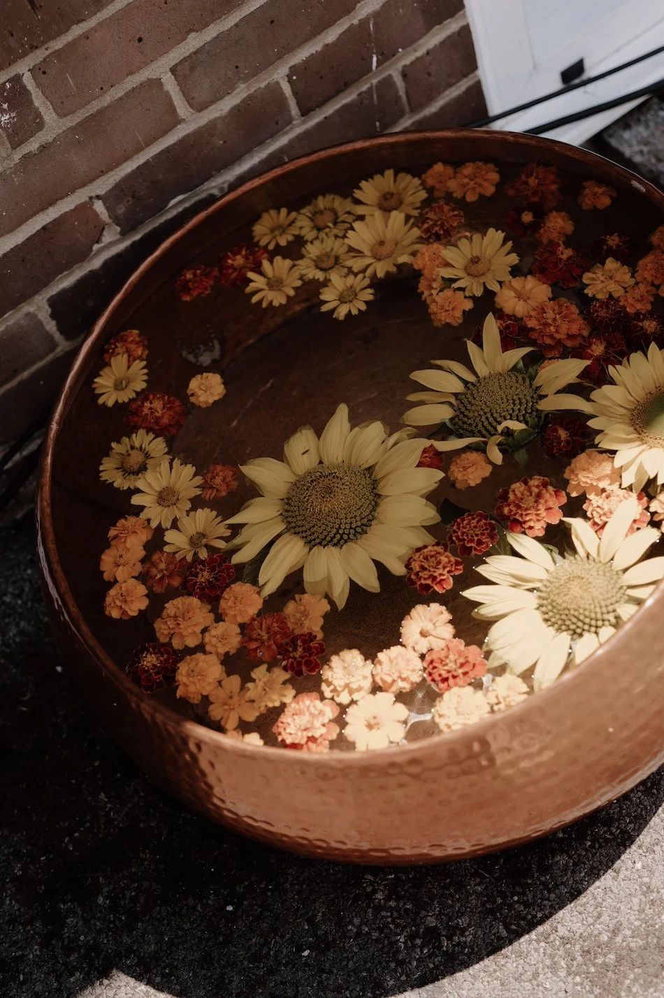 A thoughtful eco wedding detail with floating seasonal flowers in a rustic bowl, reflecting mindful, nature-inspired styling by Wild Soul Weddings, eco wedding planners in the UK. Sarah Grace Photography.