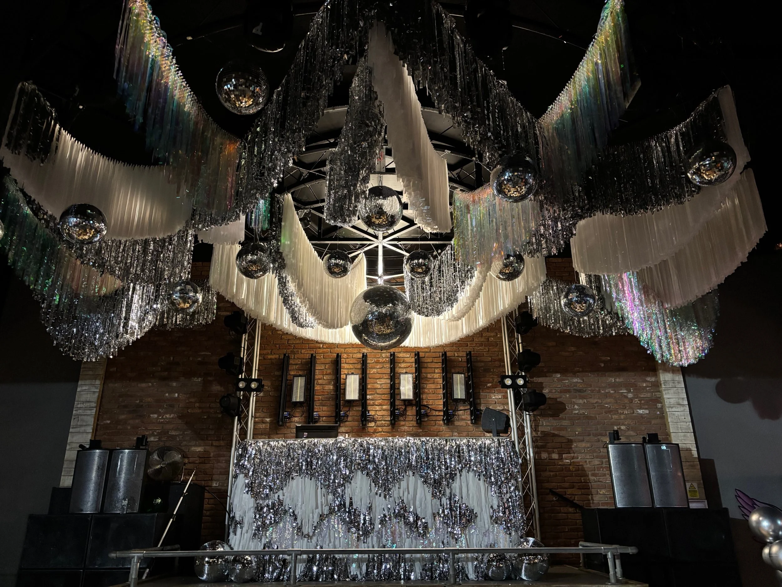Streamadelica immersive wedding décor with cascading silver and white fringe installation, mirrored disco balls and dramatic lighting, creating a glamorous, high-impact dancefloor centrepiece in an industrial venue.