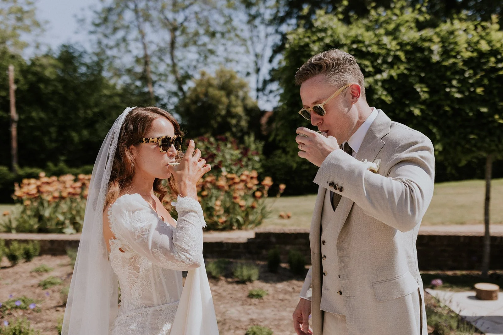 A newly married couple, both wearing shades, enjoy a drink in a sunny garden. Maja Tsolo Photography