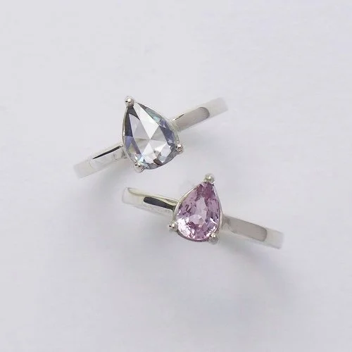 Elegant pear-cut gemstone rings in silver by Daniel Darby Jewellery Designer, featuring blue and pink stones. Handcrafted in the UK, these bespoke designs are perfect as engagement rings or modern bridal jewellery.