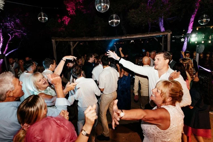 Guests dancing under disco balls and colourful lights at an outdoor wedding reception. The lively dance floor atmosphere captures family and friends celebrating together, perfect for couples wanting energetic wedding entertainment and unforgettable e