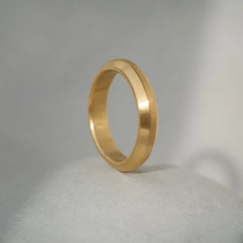 A minimalist 18ct gold contour wedding ring by Natalie Vernazza, featuring a softly polished finish and subtle curved profile, photographed on a neutral stone surface to highlight its timeless, handcrafted design.