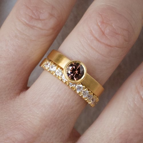 A close-up of a handcrafted yellow gold wedding ring set by Natalie Vernazza, featuring a brushed gold band with a bezel-set cognac diamond paired with a sparkling diamond eternity ring, worn together for a modern, elegant bridal look.