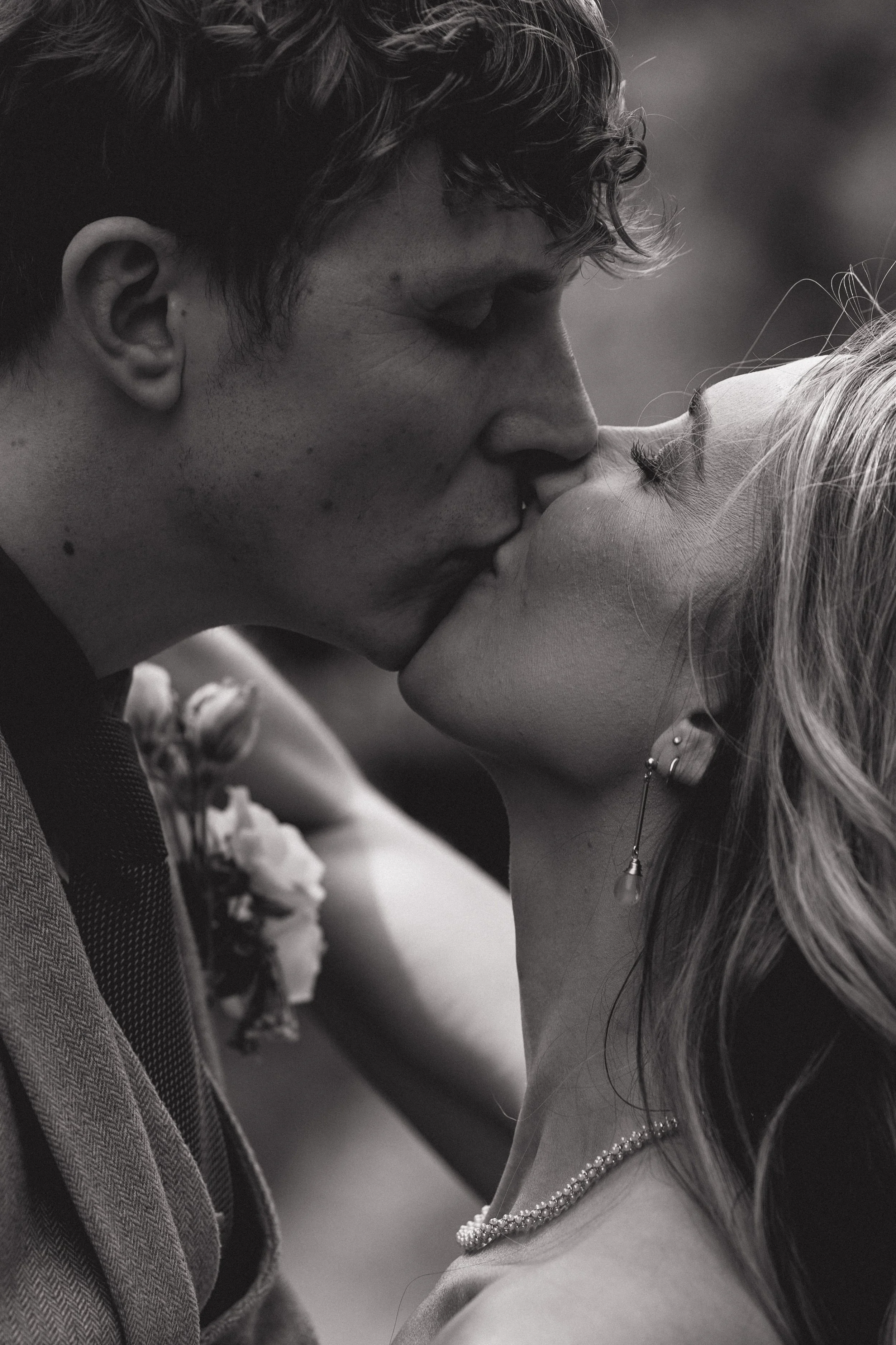 A tender and cinematic close up captured by Joy Louise Photography, showing two newlyweds sharing an intimate kiss. Their faces fill the frame as they lean into each other, eyes closed and fully absorbed in the moment. Soft natural light highlights t