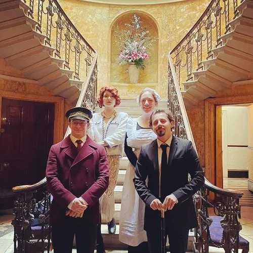 Moonstone Murders actors in full character costumes posing on a grand staircase, bringing immersive murder mystery entertainment to weddings and events.