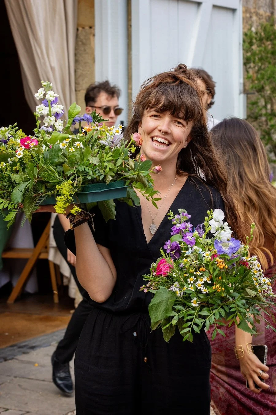 An eco-conscious wedding planner carries vibrant seasonal flowers, capturing joyful, sustainable wedding moments by Wild Soul Weddings, eco wedding planners in the UK. Martin Dabeck Photography.