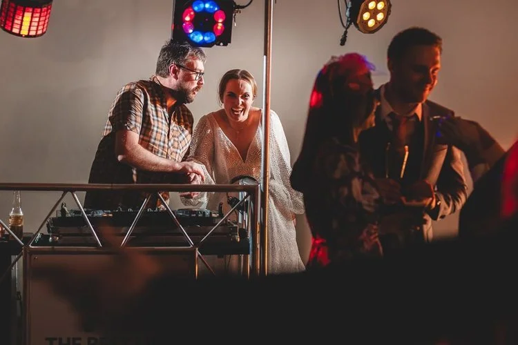 A DJ from The Best Men shares a laugh with a bride during her wedding reception, capturing the fun and friendly atmosphere that makes their performances unforgettable. With professional lighting, great music, and a packed dance floor, The Best Men de