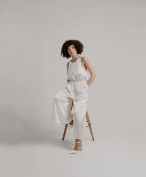Sarah Barker modern bridal jumpsuit in crisp white with wide-leg trousers and a sleeveless high-neck top, styled in a minimalist studio setting for contemporary wedding inspiration.