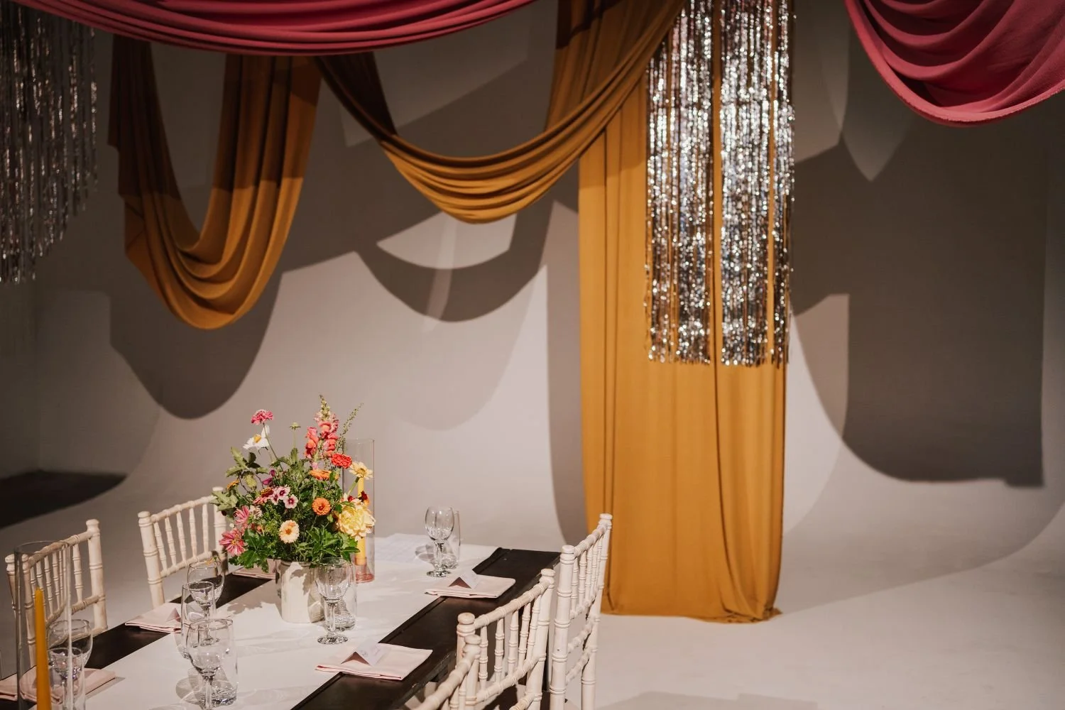 A modern wedding venue styled by Orange Tree Weddings using coloured drapes and lengths of silver foil. Photo by Lisa Jane Photography.