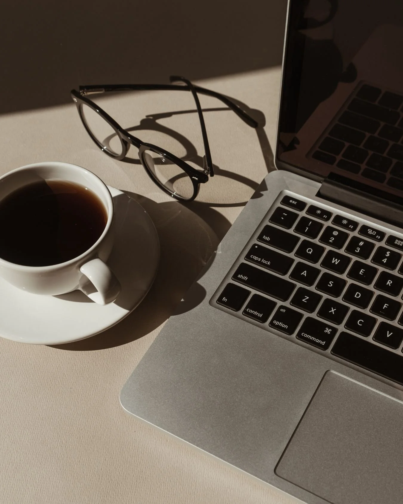 A desk set up for wedding planning and coordination with laptop, glasses and coffee.