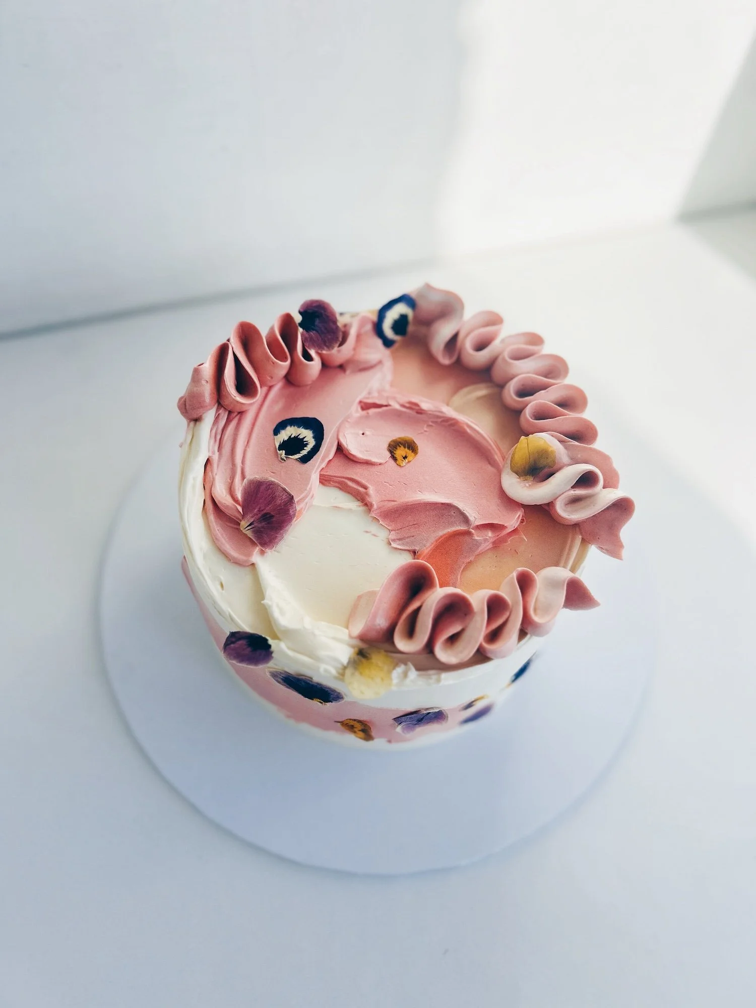 A simple celebration cake with pink swirls and flower petals.