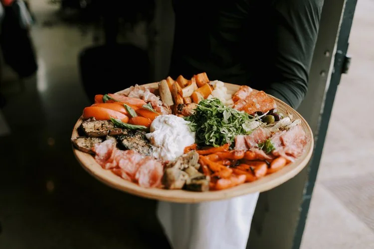 A beautifully presented antipasti platter by Tasting Plates Wedding Caterers, featuring an assortment of cured meats, roasted vegetables, fresh greens, and artisan breads. Perfect for sharing, this rustic grazing board highlights the caterer’s focus 