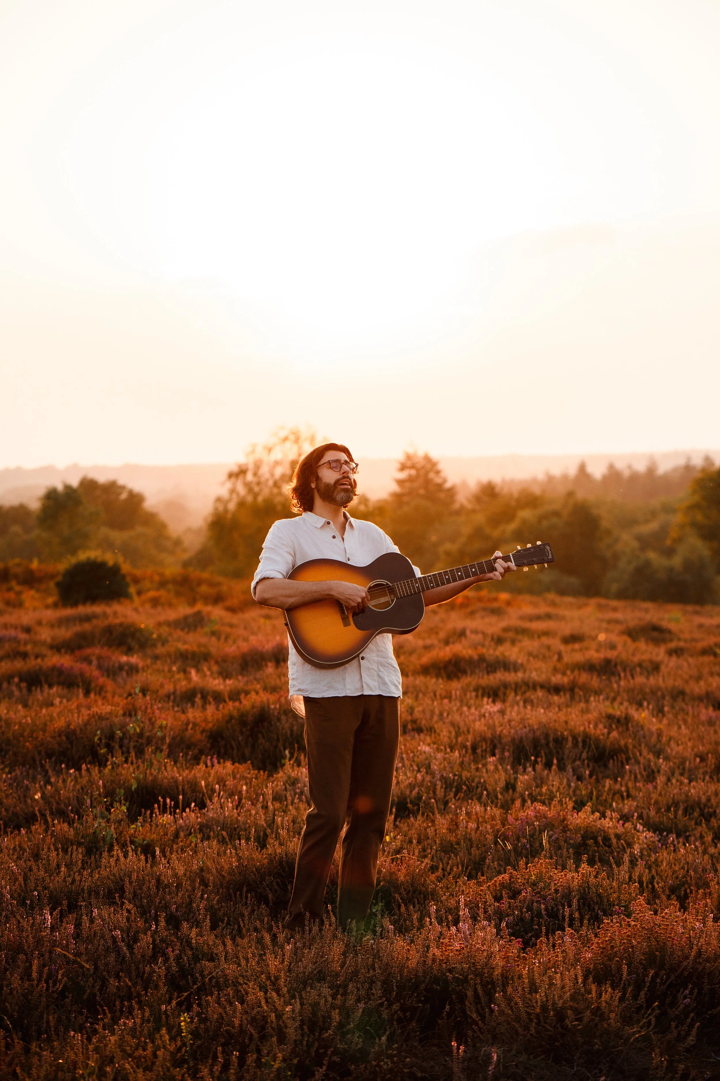 Thomas J Wilman, a singer-songwriter and acoustic wedding musician, performs with his guitar at golden hour in an open field. His soulful performance and relaxed style capture the warm, romantic atmosphere perfect for outdoor weddings and intimate ce