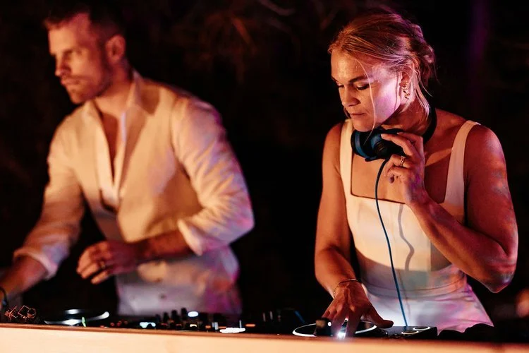 Mr and Mrs L performing live, mixing music on the decks under warm atmospheric lighting. The duo create an exciting party vibe, blending style and energy to keep the dance floor alive. Ideal entertainment for couples looking for professional DJs to d