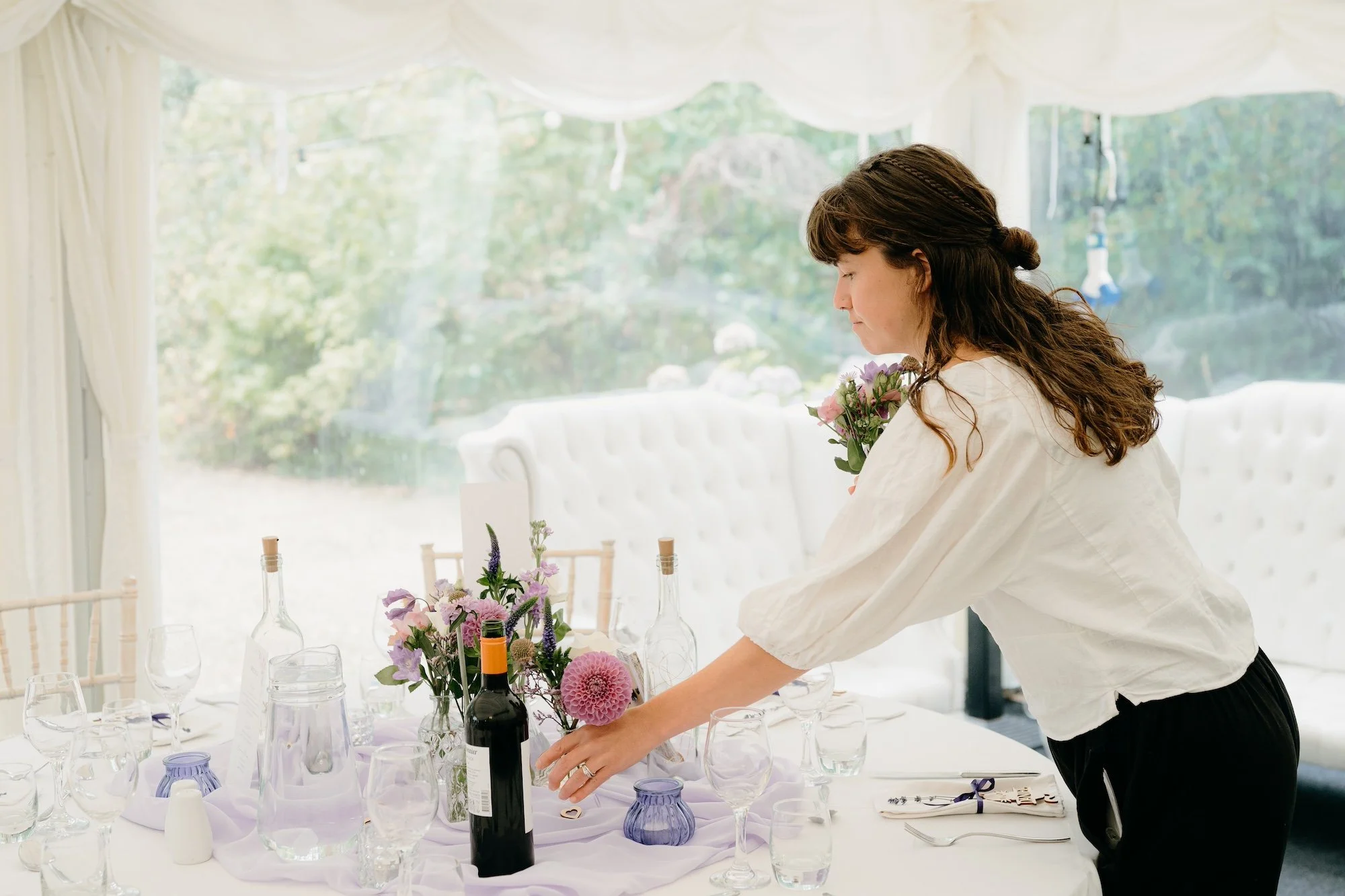 An eco wedding planner carefully styles a reception table with flowers and thoughtful details, capturing the care and intention behind a sustainably planned wedding by Wild Soul Weddings, eco wedding planners in the UK. Pip & Clo Photography.