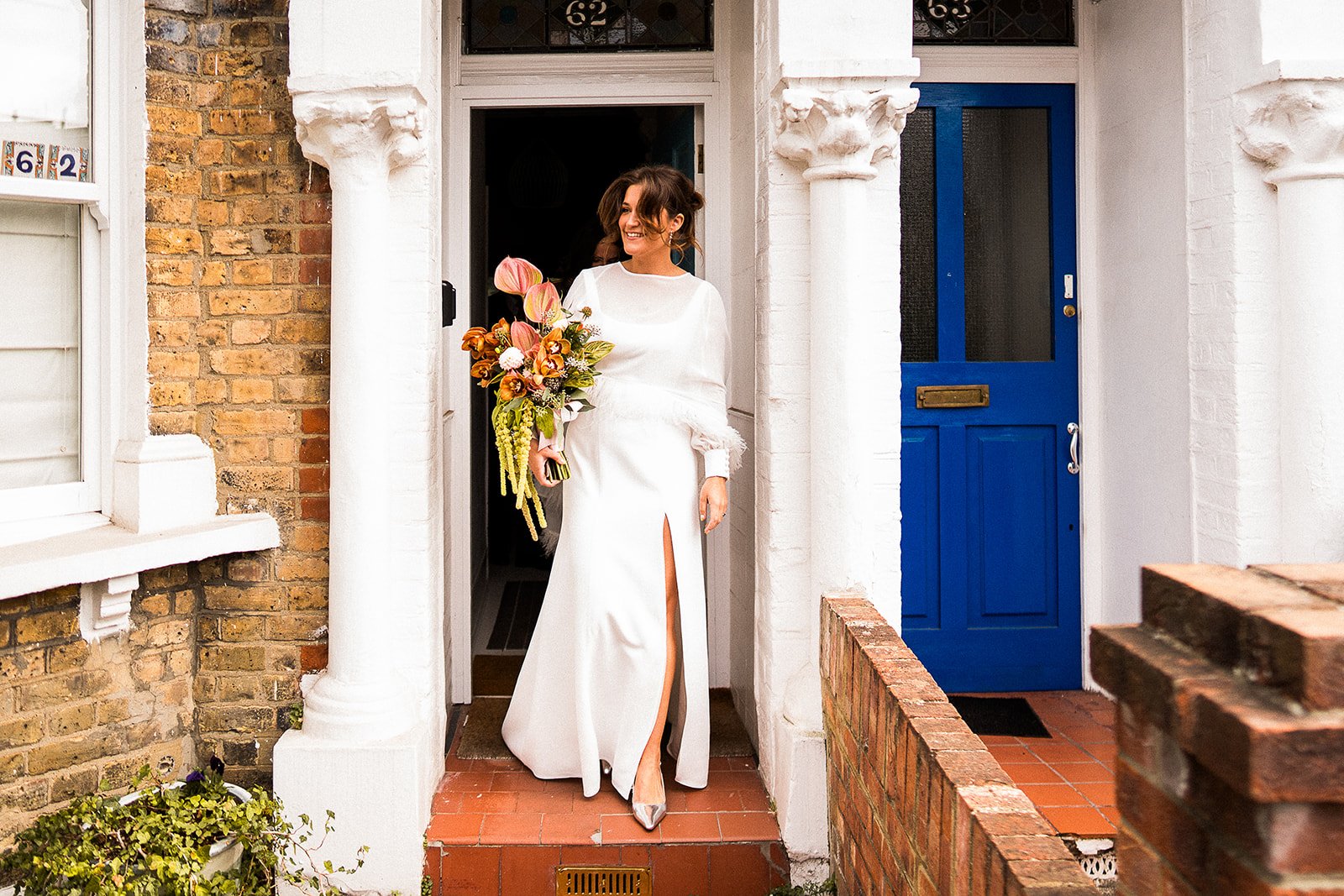 A bride leaving her house to go to her wedding. She looks happy and is holding a statement bouquet.