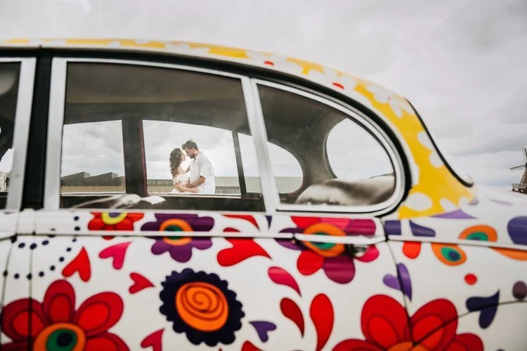 A couple embrace inside a vintage car decorated with bold floral patterns, captured by Joshua Humphrey Photography. Framed through the car window, the moment feels creative and intimate, blending quirky retro style with relaxed modern wedding storyte