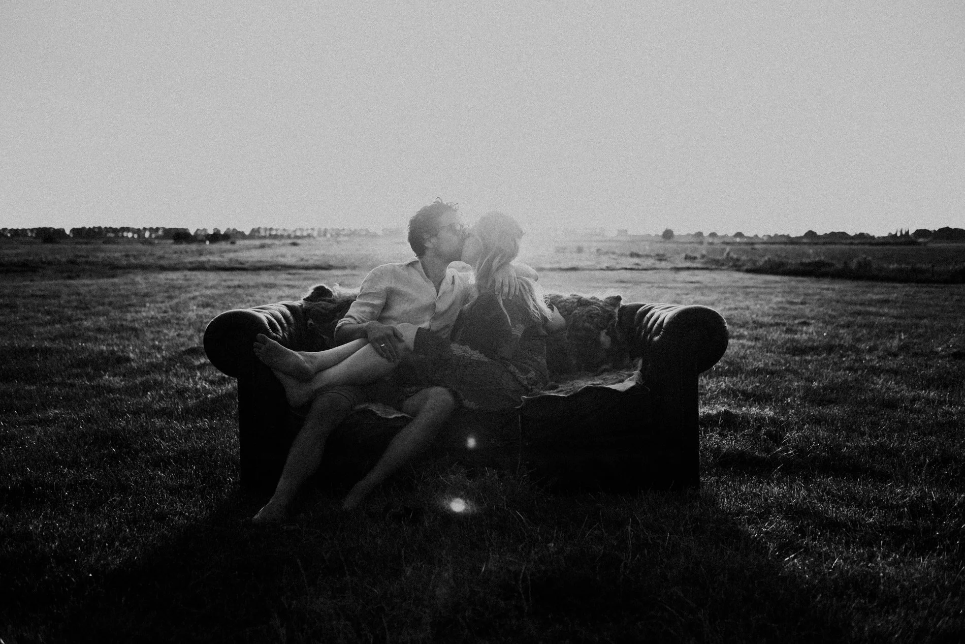 A couple share an intimate kiss on a sofa in an open field at sunset, captured in a timeless, romantic style by Quiet Mornings Wedding Photography in Scotland.