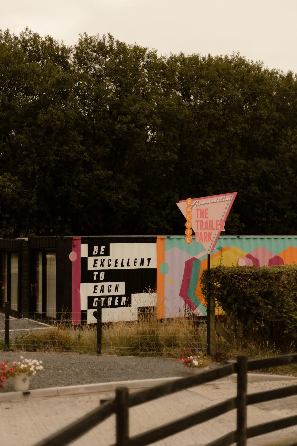 A stylish and colourful corner of The Giraffe Shed in Wales, featuring its bold on-site accommodation area known as “The Trailer Park.” The photo showcases a bold, retro-inspired pink and teal sign reading “Bougie Accommodation - The Trailer Park,” a