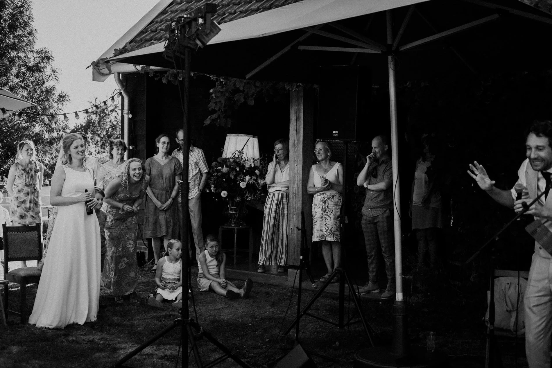 Guests laugh and react during an outdoor wedding speech, captured in candid black and white with natural emotion and atmosphere by Quiet Mornings Wedding Photography in Scotland.