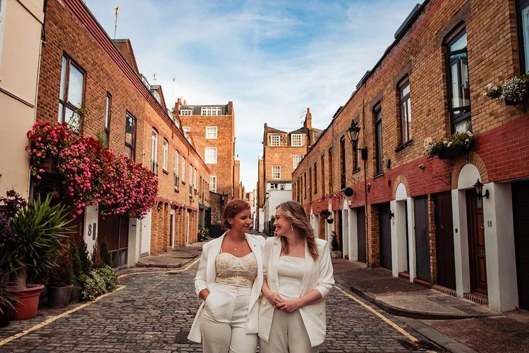 A vibrant and joyful wedding moment captured by Natalia Case Photography, showing the couple standing outside on stone steps as they celebrate with a dramatic champagne spray. The bright sunlight hits the scene from the side, illuminating the bride’s