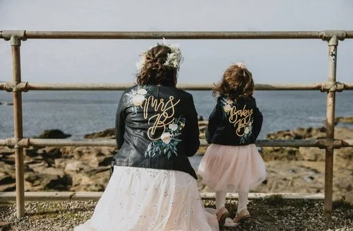 Matching hand-painted leather jackets by Bee Davies Illustration for bride and flower girl. Featuring elegant gold lettering and floral artwork, these bespoke designs add a heartfelt, stylish touch - perfect for creative brides seeking custom wedding