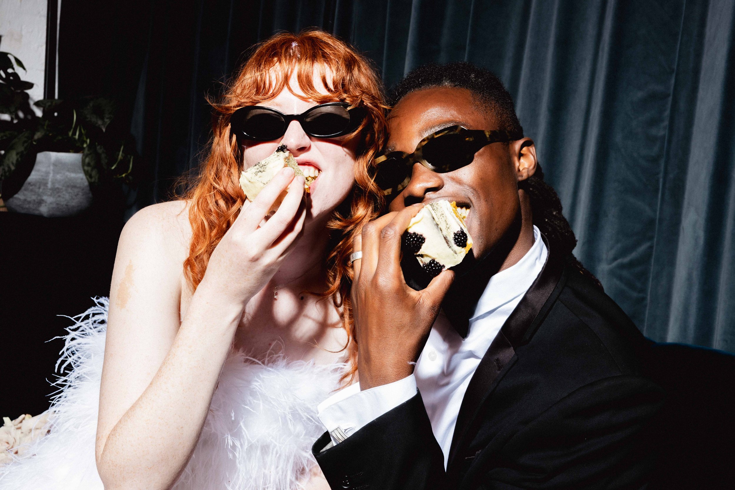 A fun, candid wedding moment at Ministry Venues, capturing a stylish couple in sunglasses enjoying cake against a luxe velvet backdrop - perfectly showcasing the venue’s modern, fashion-forward vibe for contemporary London weddings and celebrations.