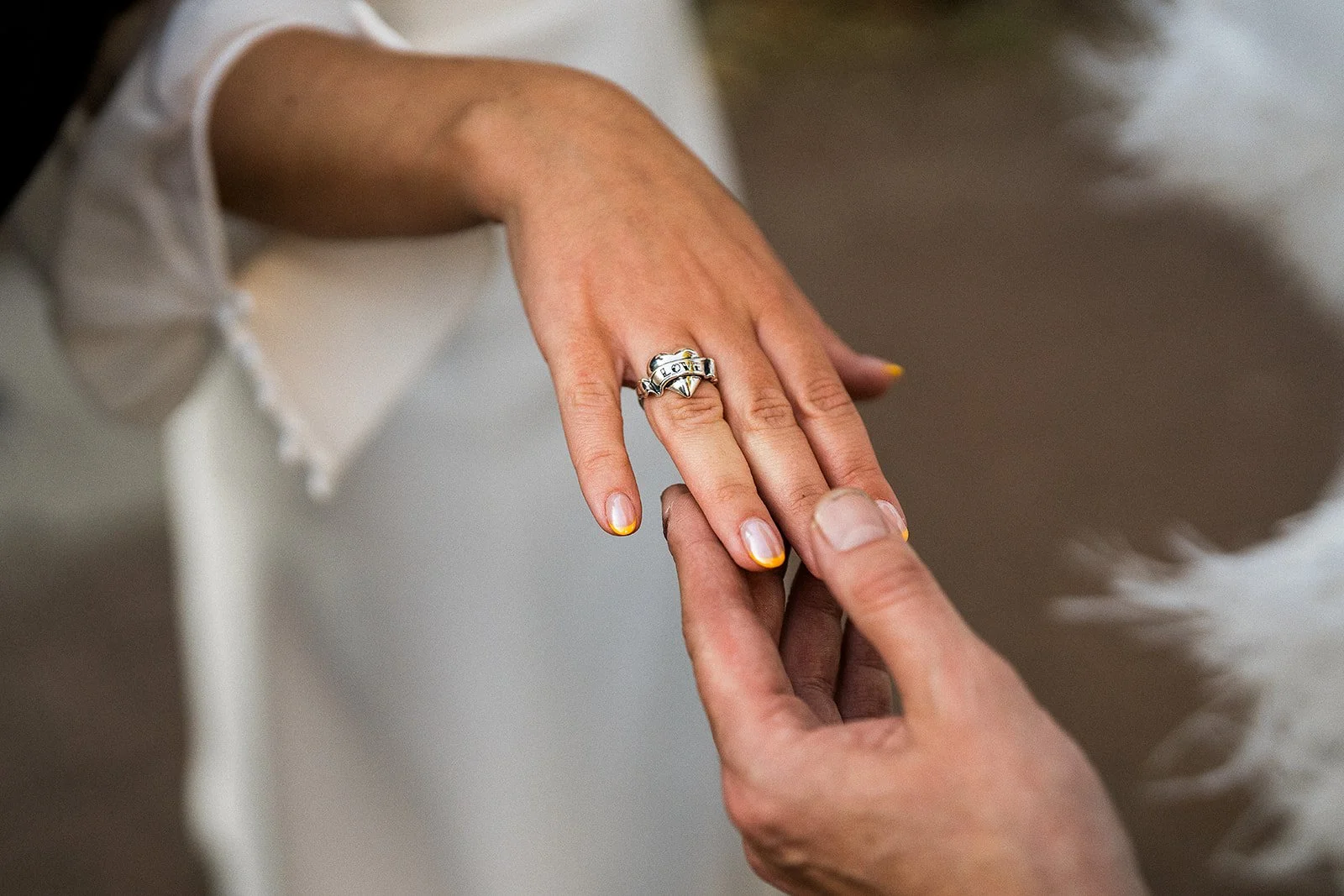 A bride wearing a heart shaped silver ring with the word LOVE on it.