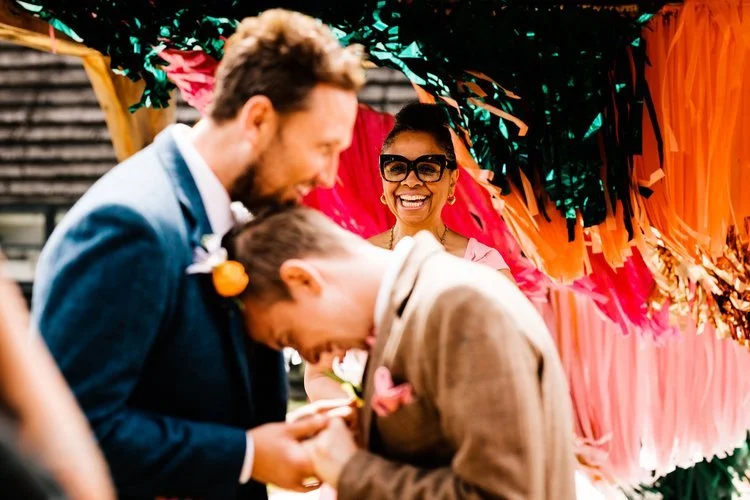 A gay wedding ceremony at The Canary Shed. The 2 grooms are holding each other and their celebrant is smiling in the background.