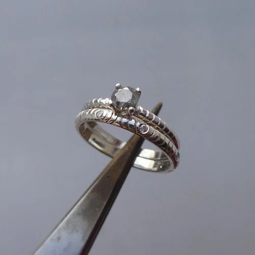 Handcrafted silver engagement and wedding ring set with a round diamond by Daniel Darby Jewellery Designer. Made in the UK, this textured band design offers a modern yet timeless look for brides seeking unique craftsmanship.