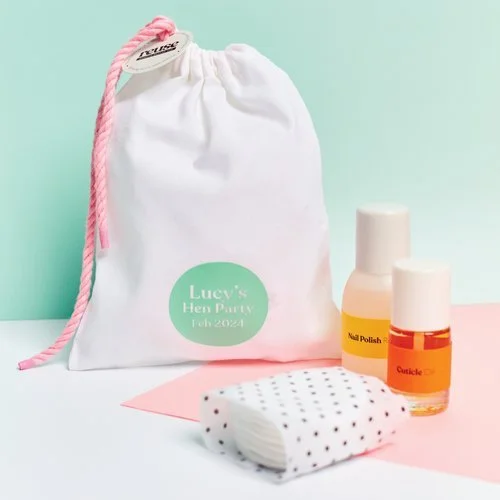 White drawstring gift bag with pink cord and green label reading 'Lucy's Hen Party Feb 2024', styled with nail care items, designed by Melon Teaspoon for custom celebration favors.