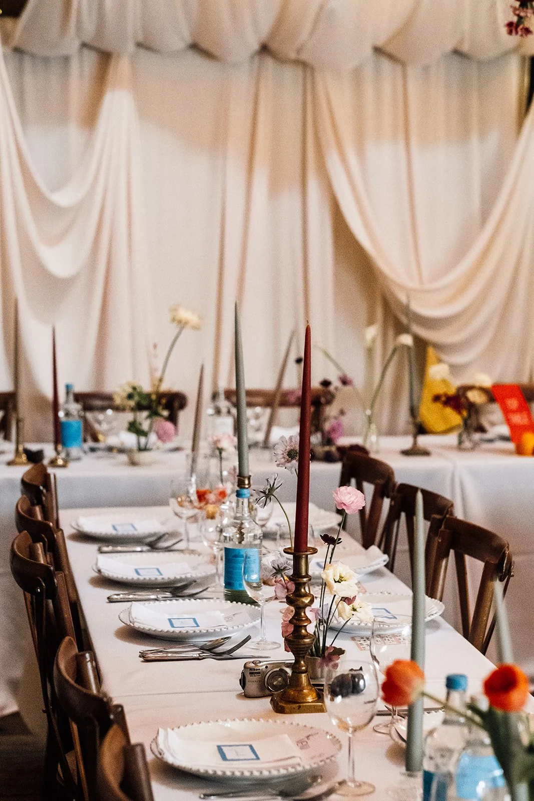 Orange Tree Weddings styling and décor featuring an elegant long-table wedding setup with soft draped backdrops, pastel taper candles, delicate florals and relaxed place settings, creating a romantic, contemporary wedding tablescape.