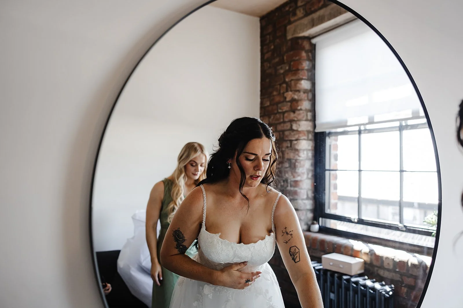A reflection in a mirror of Marie the bride gets ready for her wedding, with some help from one of her bridesmaids.