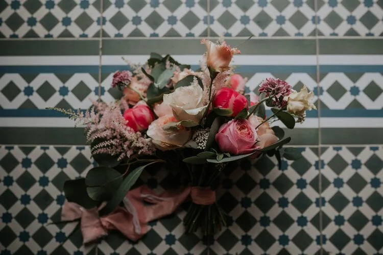 Romantic wedding bouquet by Catherine Short Florals featuring pink peonies, blush roses, astilbe and soft greenery tied with flowing silk ribbon. Styled against patterned vintage tiles, this vibrant modern arrangement highlights Catherine Short Flora