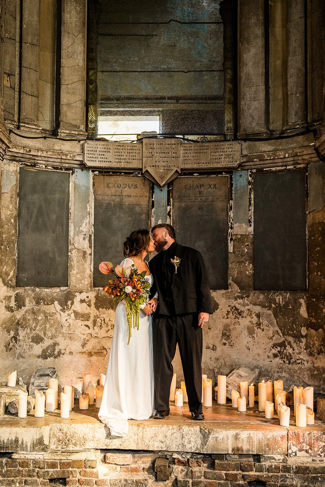 A bride and groom portrait inside the Asylum Chapel. They are kissing and they are surrounded by candles.
