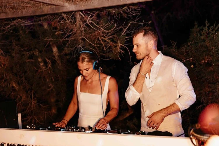 Mr and Mrs L performing at an outdoor reception while guests dance and celebrate under disco balls and colourful lighting. The lively setup blends professional sound equipment with a fun festival-style atmosphere, perfect for couples wanting high-ene
