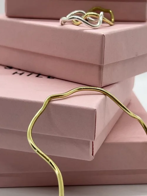 Elegant wavy gold and silver rings by Stacey Hill Jewellery displayed on soft pink gift boxes. Perfect for modern brides seeking minimalist, handcrafted wedding jewellery made in the UK.