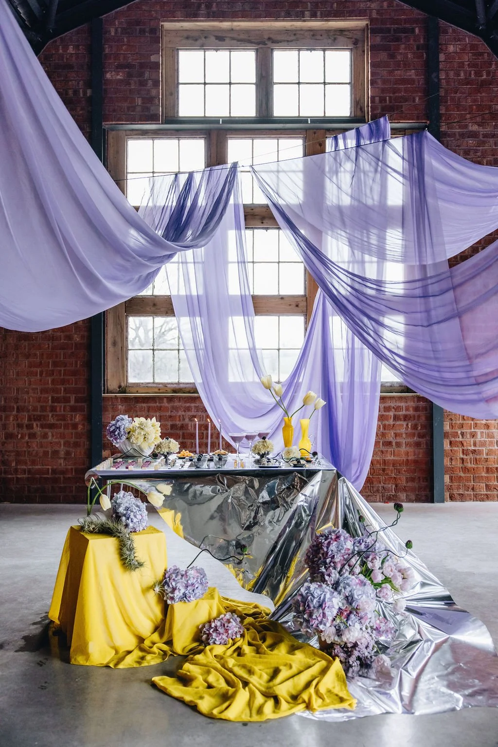 Orange Tree Weddings styling and décor showcasing soft lilac draping, reflective metallic tablescape and sculptural florals, creating a contemporary, editorial-style wedding setting inside an industrial brick venue.