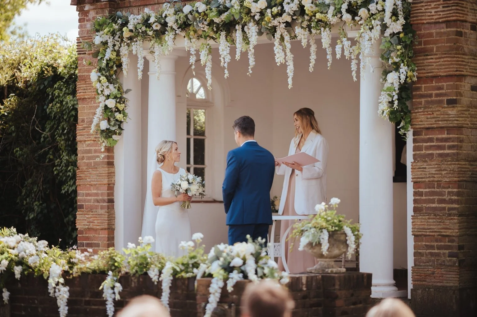 A beautiful celebrant-led wedding ceremony. There are white flowers and the bride and celebrant are both wearing white.