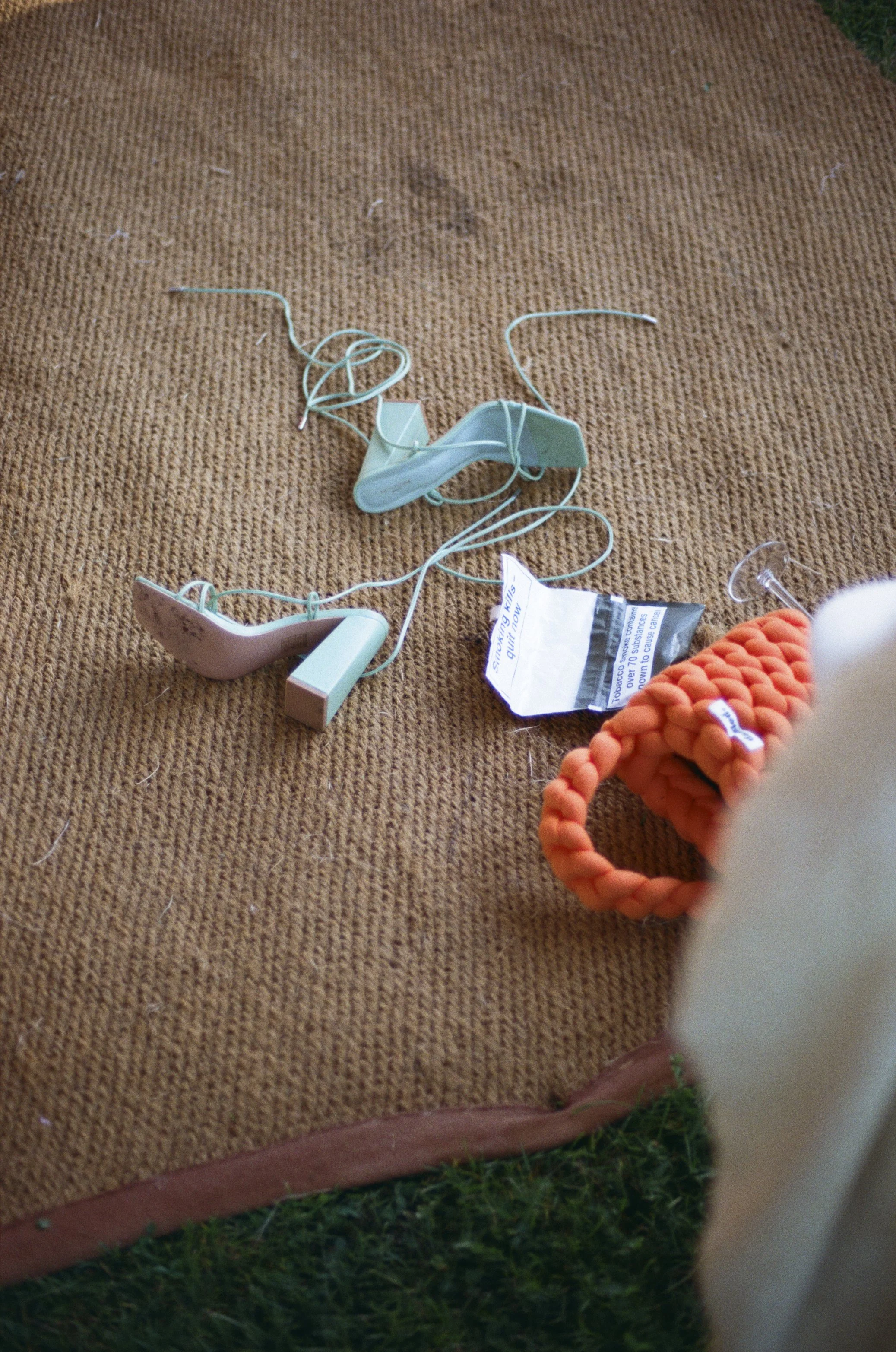 A pair of mint green heels and a bright orange woven bag lie on a rustic mat during wedding preparations, captured by Roz Pike Photography. The candid detail shot highlights the relaxed colourful styling and behind-the-scenes charm of a modern outdoo