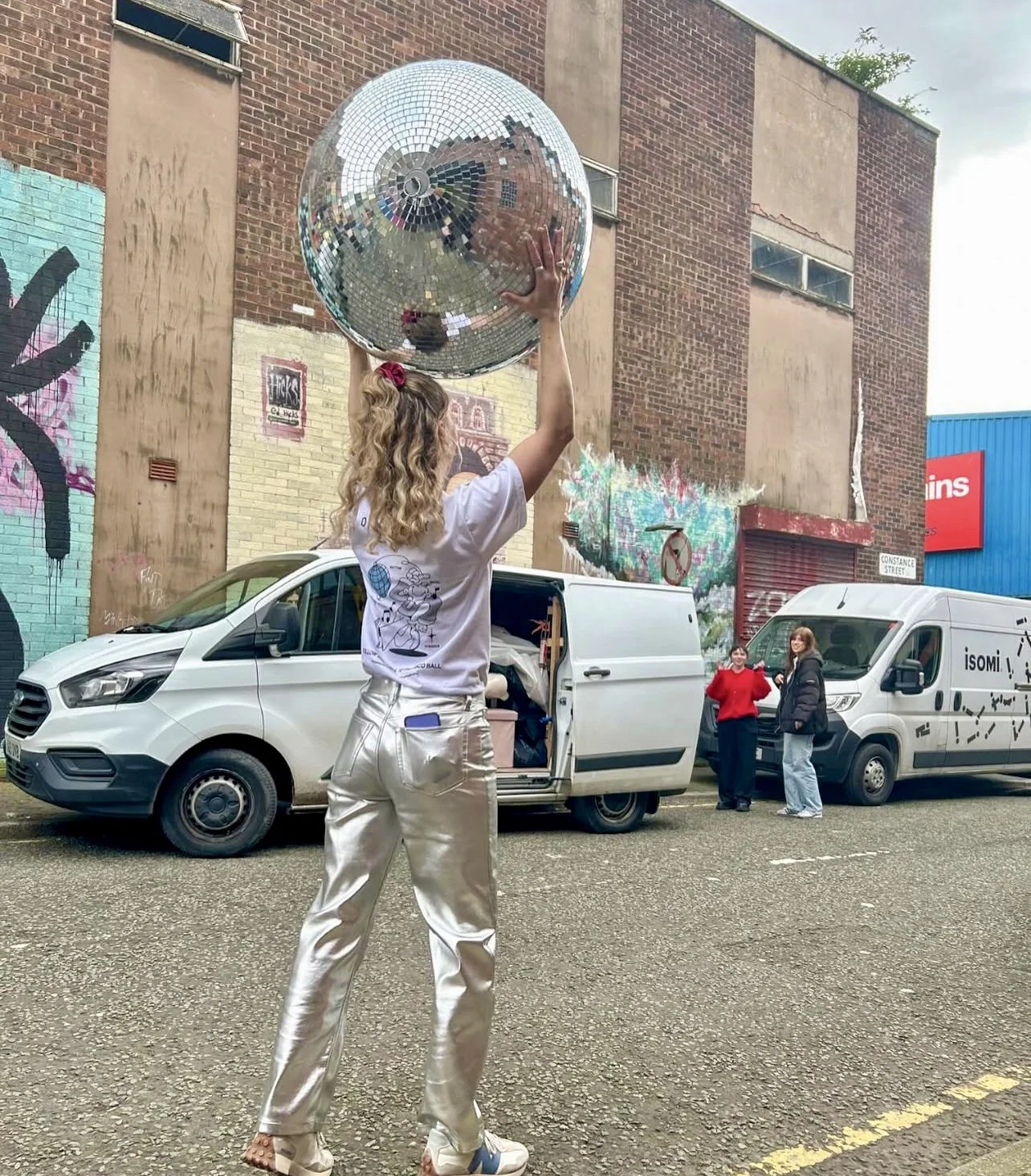 A female wedding supplier holding up a giant disco ball. she is wearing silver trousers.