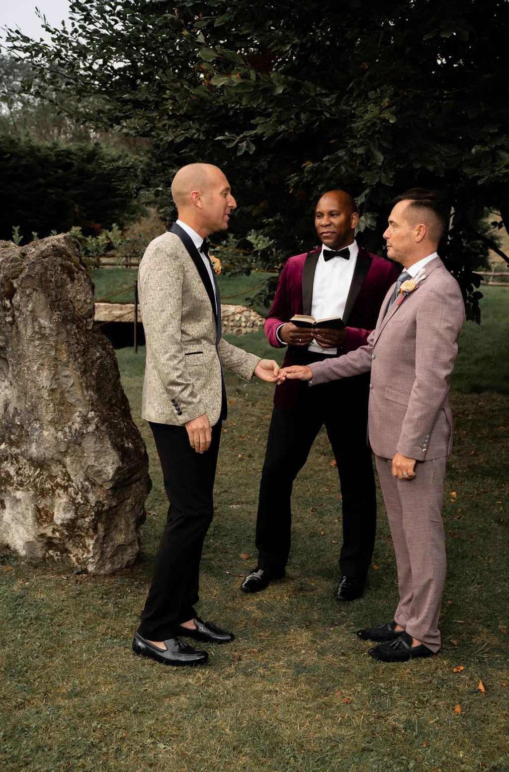 Dave Octave Celebrant in a maroon blazer, with 2 grooms during a same sex wedding ceremony. The grooms are holding hands and sharing a heartfelt moment.