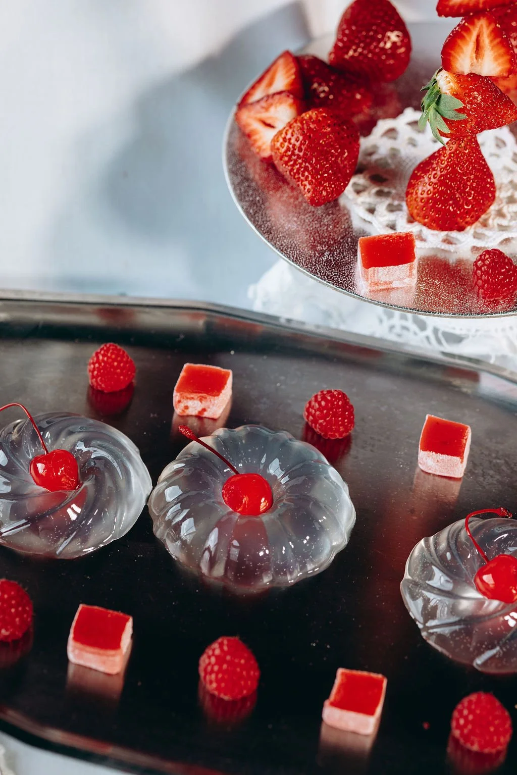 Orange Tree Weddings styling and décor showcasing modern dessert styling with clear jelly moulds, fresh cherries, strawberries and raspberry sweets, styled on mirrored trays for a bold, contemporary wedding tablescape.