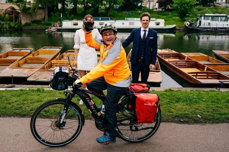 80's kids TV icon Timothy Mallet, enthusiastically poses for the camera whilst on a bike, as a newly married couple laugh behind him along a riverside path, captured with humour and perfect timing by Jordanna Marston Photography. The colourful cyclin