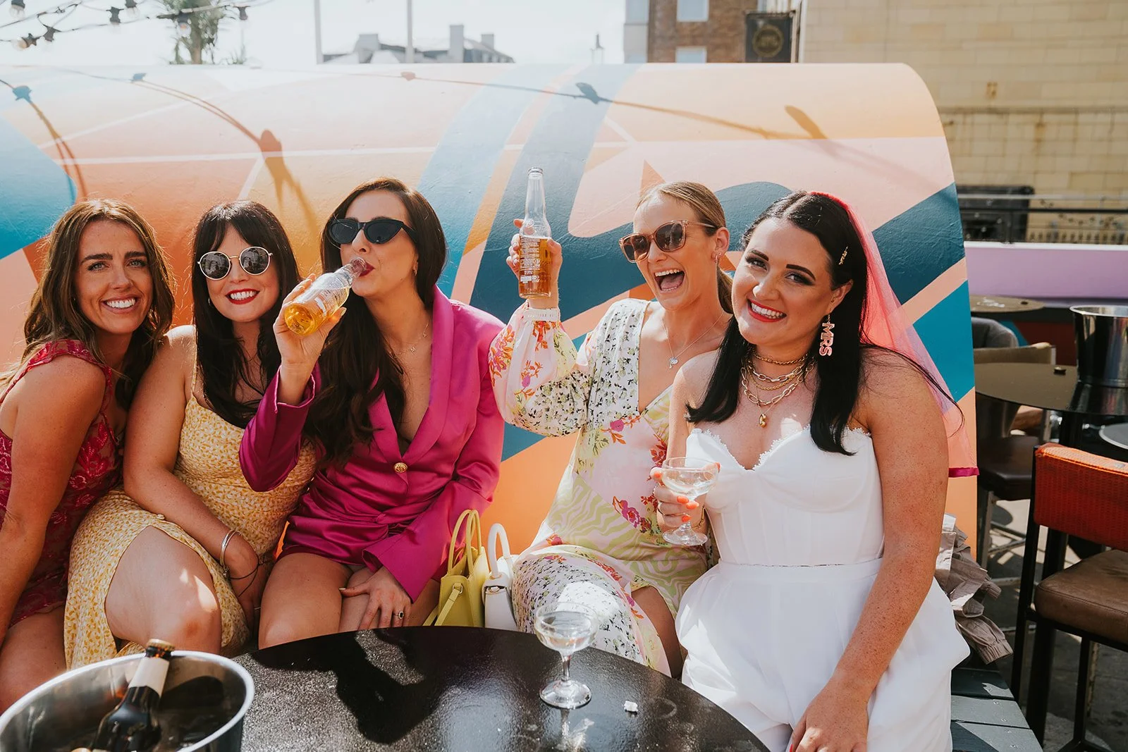 Bride and friends enjoy drinks outdoors at Pier Court Wedding Venue in Brighton, capturing a fun, relaxed seaside wedding celebration in the sunshine.
