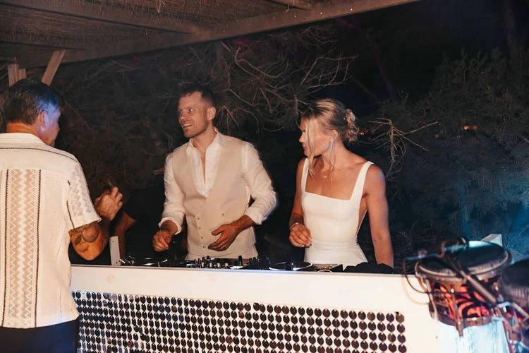 Mr and Mrs L performing at an outdoor reception while guests dance and celebrate under disco balls and colourful lighting. The lively setup blends professional sound equipment with a fun festival-style atmosphere, perfect for couples wanting high-ene