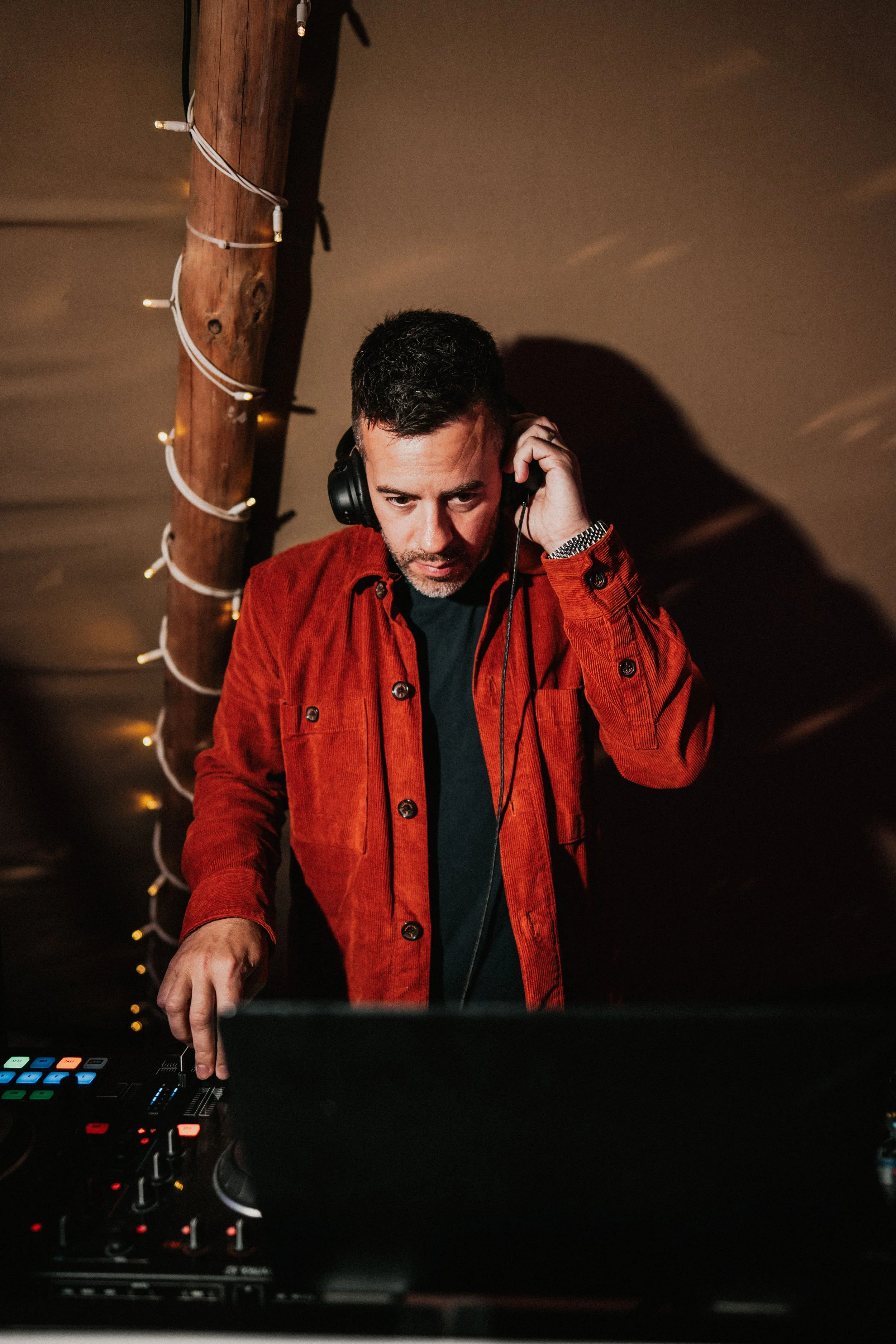 A professional wedding DJ from Married to the Music performs live at a wedding celebration, wearing a bold red jacket and using high-end DJ equipment. Warm lighting and rustic wooden decor create an inviting party atmosphere for the evening reception