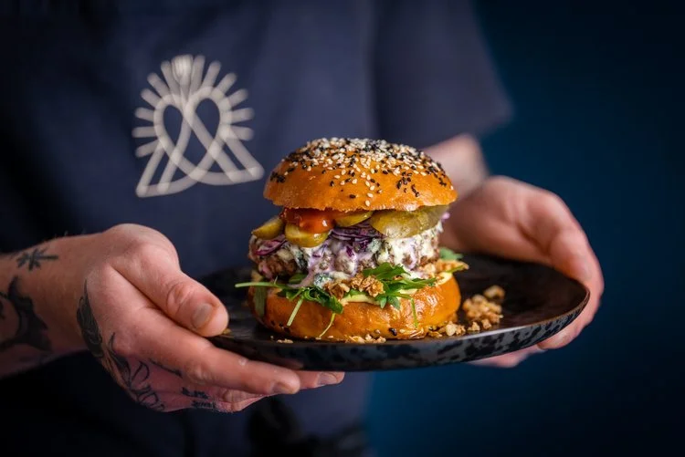 A gourmet burger prepared by Hardy’s Catering, served on a black plate with a perfectly toasted sesame seed bun, fresh rocket, crunchy pickles, and creamy slaw. This close-up food photography highlights Hardy’s commitment to delicious, high-quality i