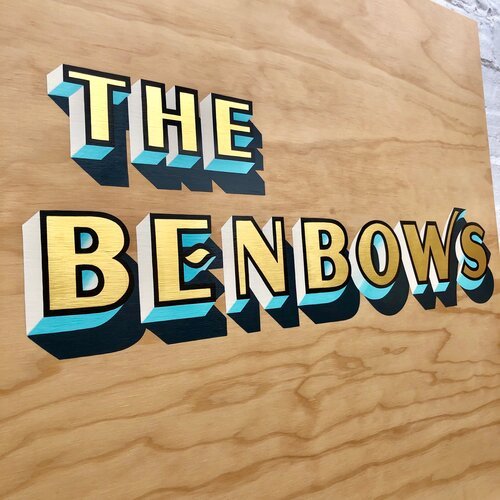 A beautifully hand-painted custom wooden sign by Esther of Sylvie Signs reading “The Benbows.” The design features bold 3D lettering in cream, turquoise, and gold tones with a black shadow for depth, set against a smooth natural woodgrain background.