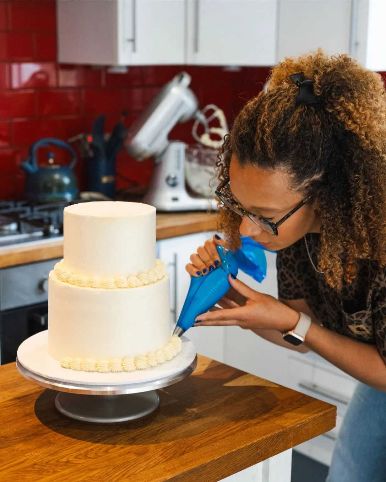 London wedding cake maker The Cake Hun piping vintage buttercream detailing onto a tiered wedding cake. A modern, design-led cake studio specialising in retro-inspired wedding cakes, elegant finishes, and handcrafted celebration cakes for creative, c